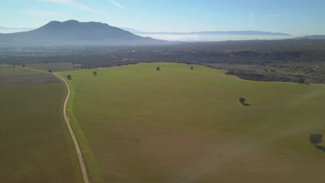 Luftaufnahme-Einer-Ausgedehnten-Wiese-An-Einem-Sonnigen,-Dunstigen-Tag-Mit-Bergen-Im-Hintergrund