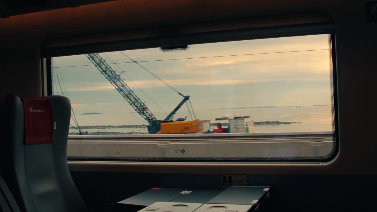 Vista da janela de um trem em movimento mostrando a lagoa de Veneza e uma van branca dirigindo em uma estrada paralela. Filmagem de viagem do trânsito pela ponte em direção à histórica cidade italiana.