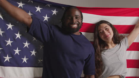 studio portrait shot of multi-cultural couple holding american flag behind them celebrating 4th july independence day 3