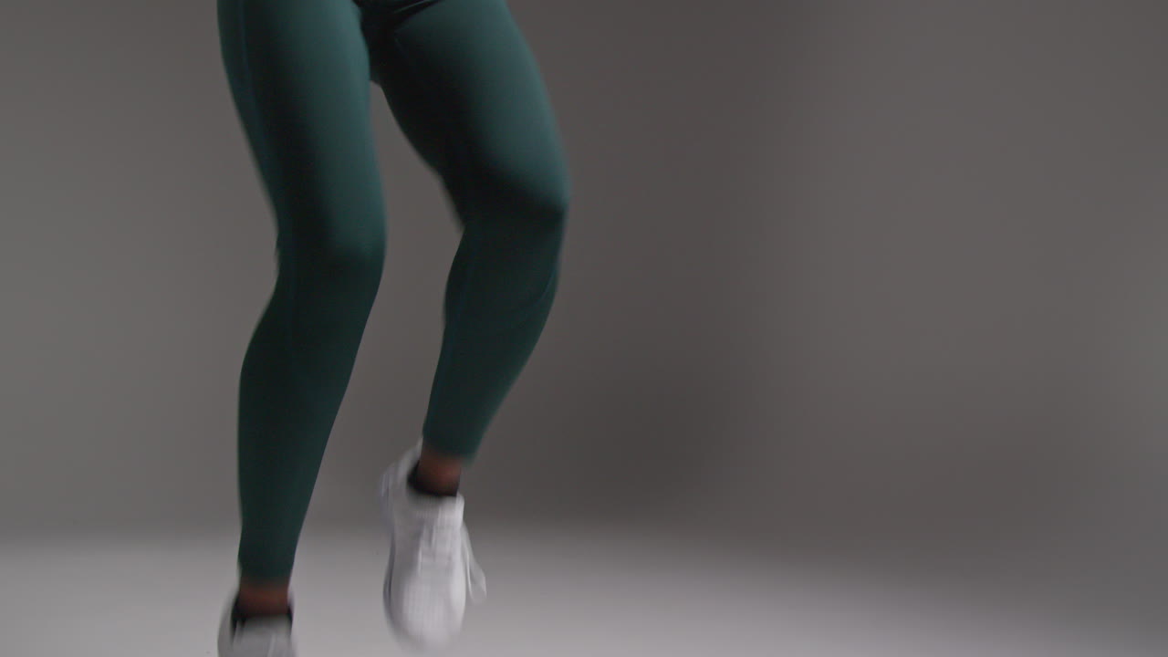 fotografía de bajo ángulo de una atleta que lleva un traje de entrenamiento en una clase de gimnasia corriendo en el lugar contra un fondo plano 1