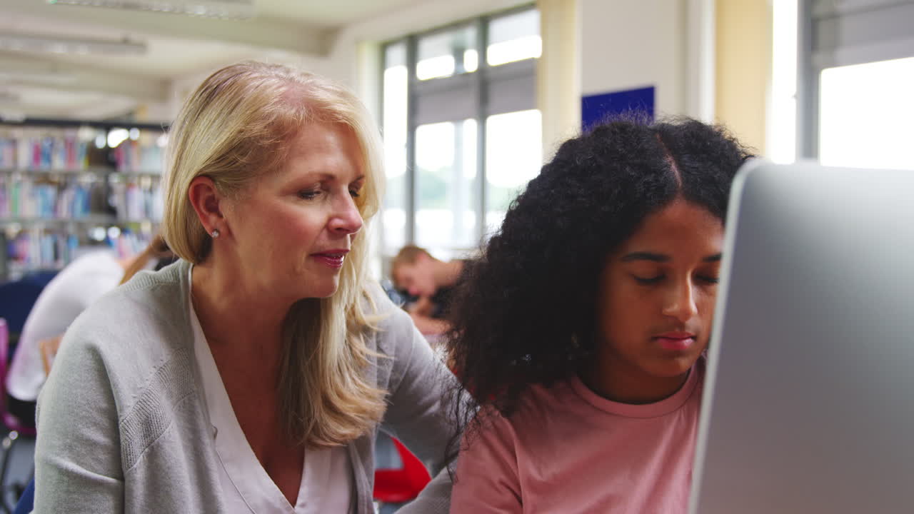maestra con una estudiante que trabaja en una computadora en la biblioteca de la universidad