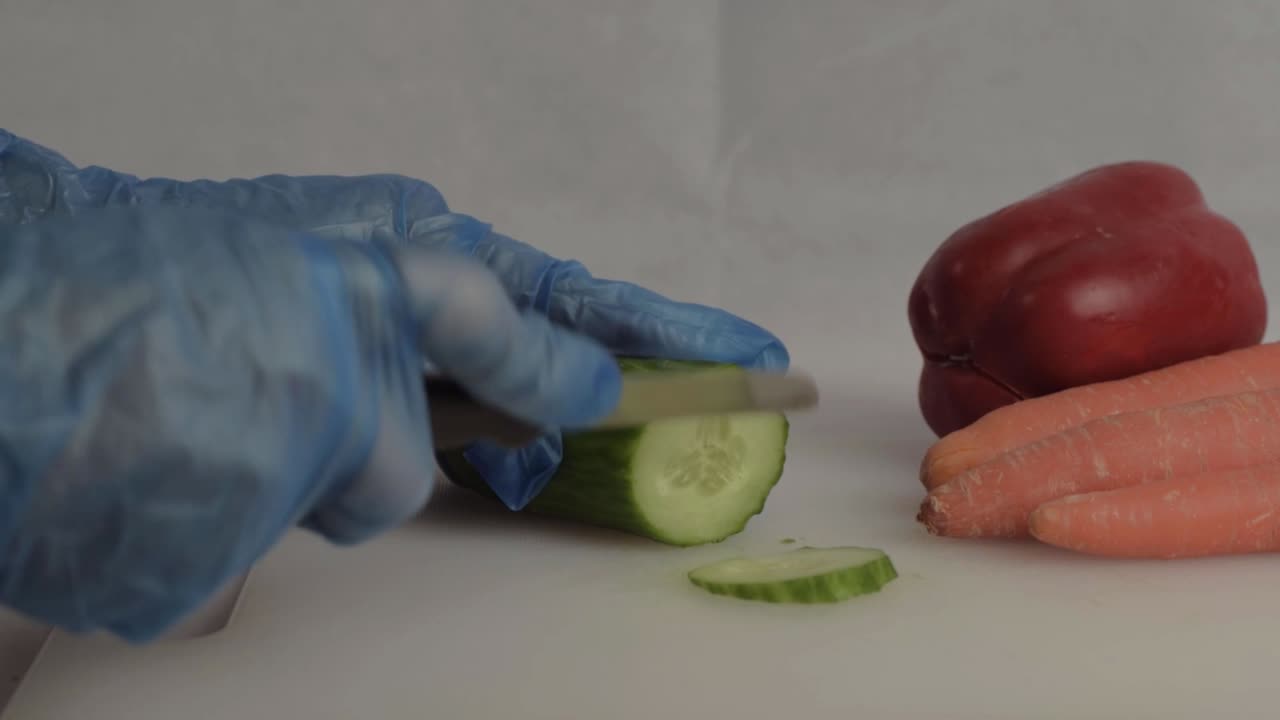 Hånd med blå hygienehansker som skjærer en agurk med vegetabilsk bakgrunn