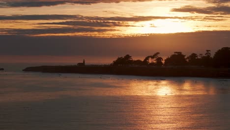 Stationäre-Drohnenaufnahme-Des-Farbenfrohen-Sonnenuntergangs-Zur-Goldenen-Stunde-Und-Der-Surfer