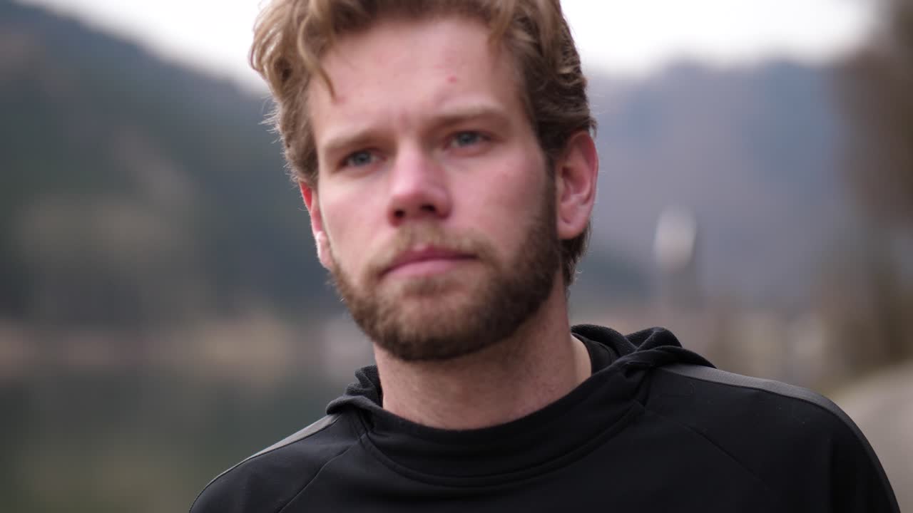 aquí se puede ver a una joven rubia concentrada con ropa deportiva negra caminando junto a un río entre pequeñas colinas