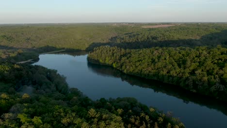 Drone-shot-at-high-altitude-of-a-lake-in-the-mountains-surrounded-by-thick-forest-in-Wisconsin,-USA,-during-sunset