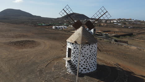 Aerial-shot-in-orbit-over-an-old-cereal-mill-on-the-island-of-Fuerteventura,-displaying-the-mountains-around-Villaverde-city