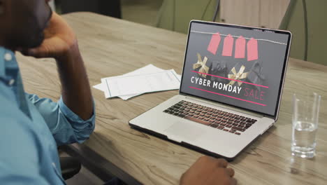 african american man at table using laptop, online shopping on cyber monday, slow motion