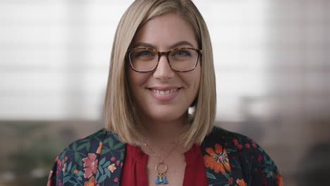 close up portrait of friendly blonde business woman smiling happy looking at camera wearing glasses in office workplace background