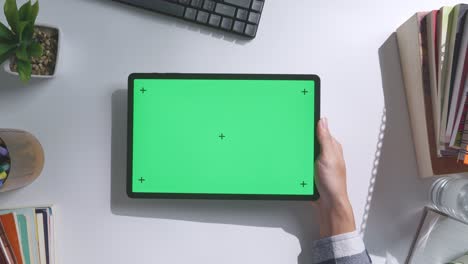 top down view of a laptop computer with mock up green screen chromakey display on a wooden office desk next to notebook with pens, glasses, and a glass of water. slow zoom out, close up