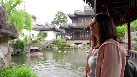 Woman-standing-next-to-a-pond-under-a-corridor-in-Yuyuan-Garden,-Shanghai