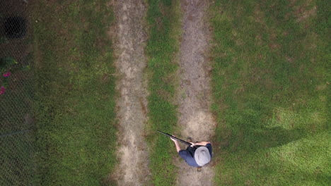 Aerial-view-looking-straight-down-on-a-man-carrying-a-shotgun-in-the-ready-position-walking-into-the-frame,-stopping-halfway-he-raises-the-pump-action-shotgun-and-cocks-it-then-walks-out-of-frame