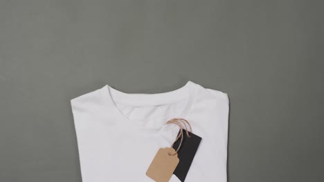 Video-of-flat-lay-of-white-t-shirt-with-tags-and-copy-space-on-grey-background