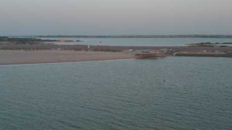 cinematic drone - aerial panorama circling shot a windsurfer and buggykiting at sunset with tourists and people at zeeland at the north sea, netherlands, 25p