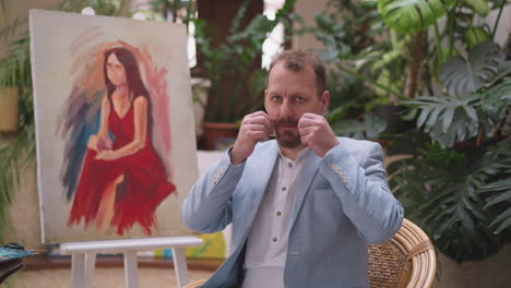 a man in a blue blazer posing with a painting in his studio