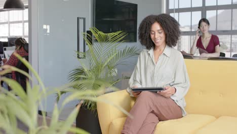 Portrait-of-happy-diverse-casual-businesswoman-using-tablet-sitting-on-sofa-in-office,-slow-motion