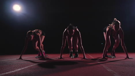 Female-runners-at-athletics-track-crouching-at-the-starting-blocks-before-a-race.-In-slow-motion.