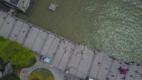 overhead aerial descends to people strolling shanghai river waterfront