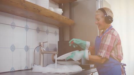 positive senior woman cleaning dirty plates and listening to music in headset