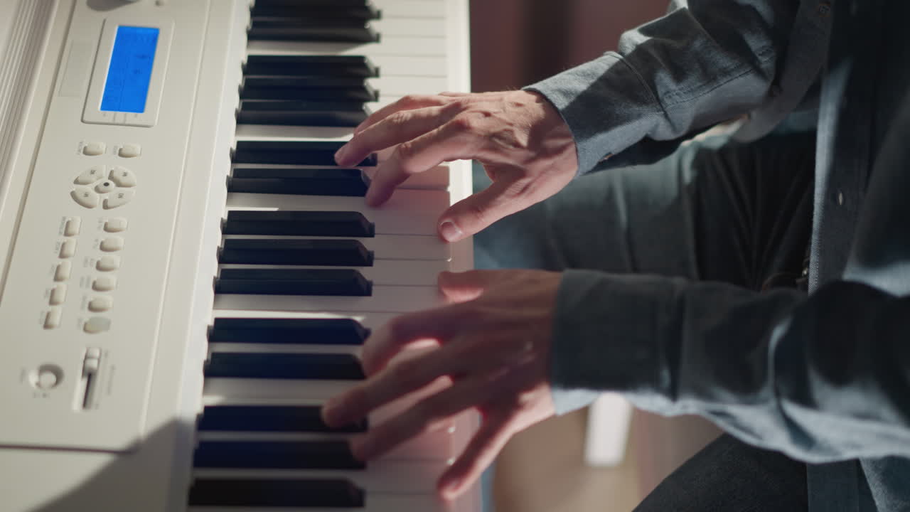 하 피아노를 연주하는 파란색 장갑 셔츠를 입은 남자의 손의 클로즈업. 손가락과 키 사이의 상호 작용에 초점을 맞춘 세부 사항과 함께 음악 창조의 순간