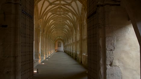 View-through-an-old-medieval-doorway-along-the-quiet,-atmospheric,-arched-cloisters-in-the-beautiful-medieval-cathedral-of-Wells,-in-England's-smallest-city