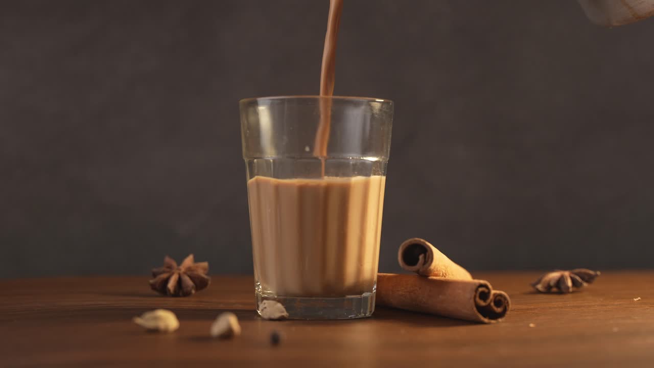Chai indiano servito in tazze di vetro, preparato in un bollitore di metallo con masalas aromatici. Viene versato nel vetro.