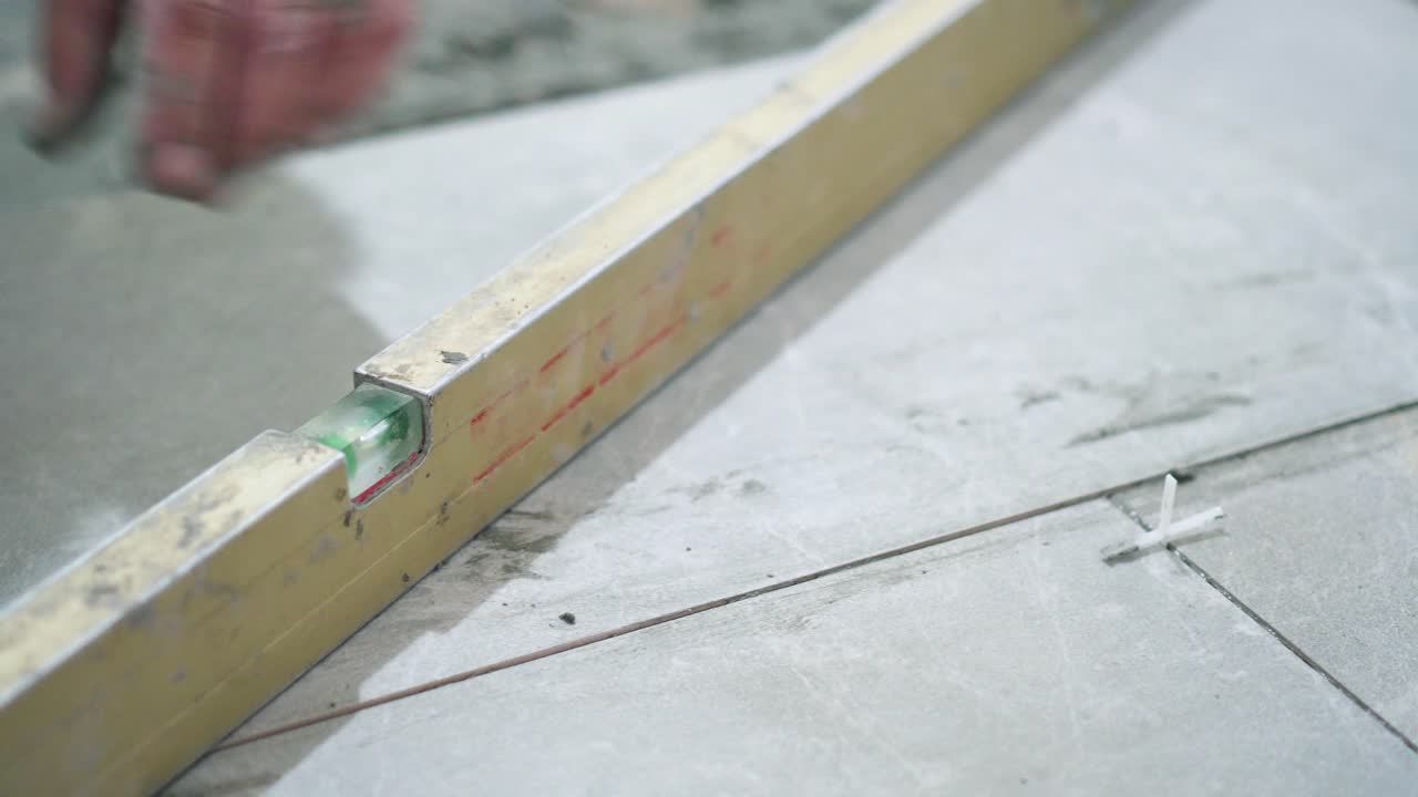 A close look at the construction tiler worker laying down the tile on cemented floor. Professional worker laying tiles on floor at construction site close-up slow motion.