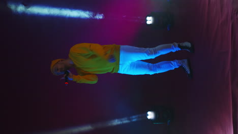 video vertical. cantante divertido incendiario con ropa amarilla bailando y cantando con un micrófono de color neón. saltar y moverse vigorosamente. artista de hip-hop y pop