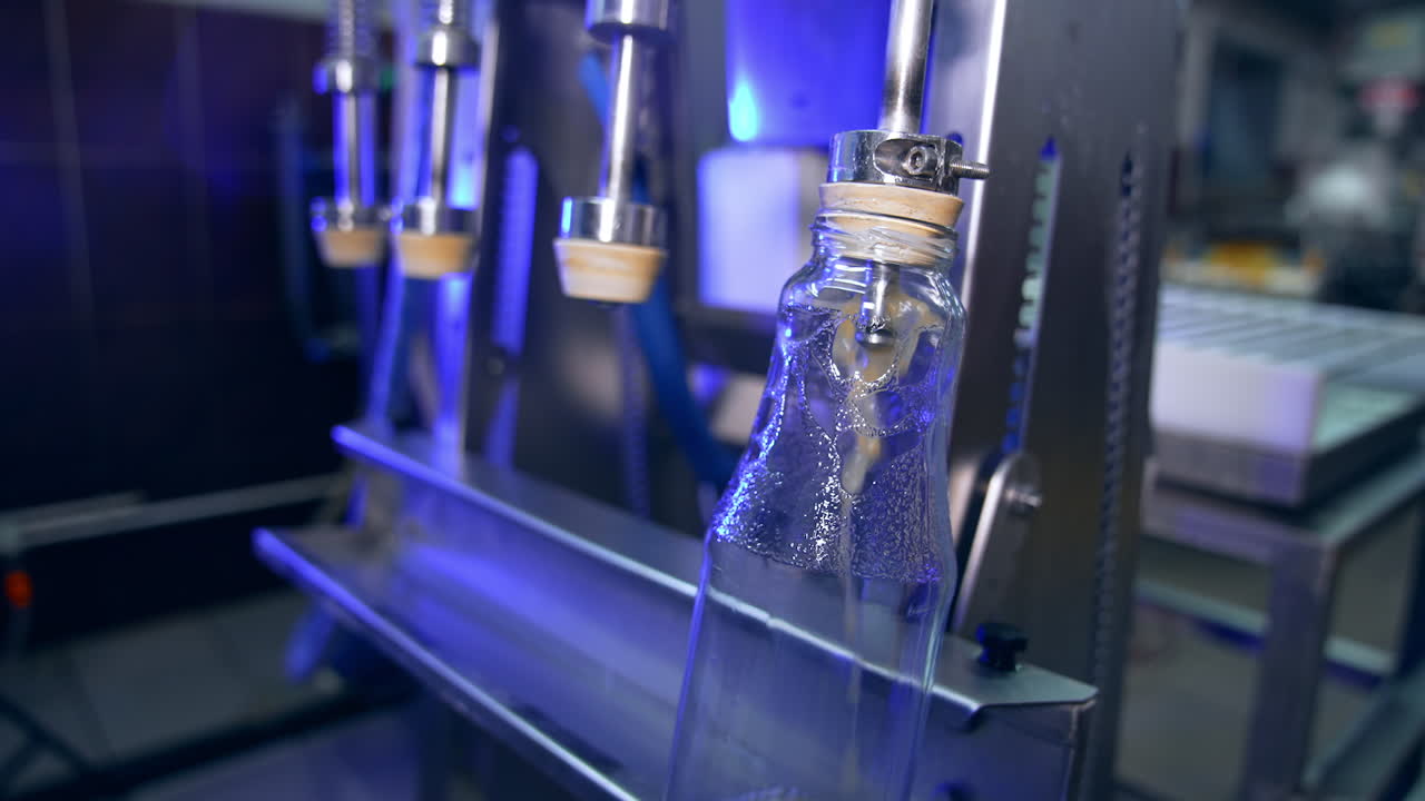 Glass bottles being filled with freshly-squeezed apple juice. Close up. Automated system for manufacturing organic food.