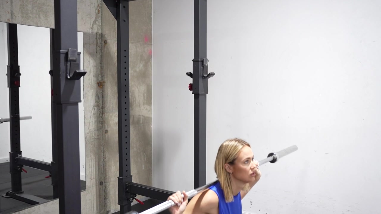 A woman is doing squats with a barbell in her home gym to enhance fitness and strength