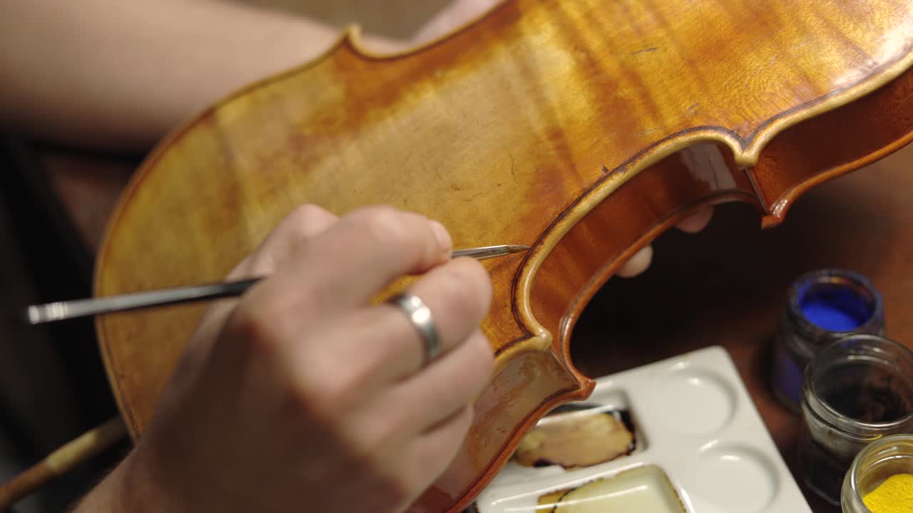 Focused luthier varnishing violin in workshop