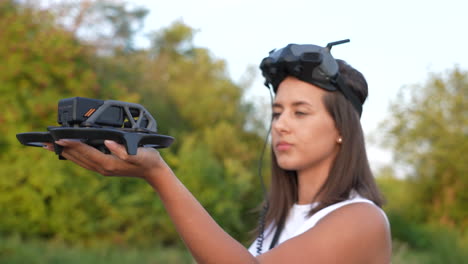 Primer-Plano-De-Una-Mujer-Joven-Con-Auriculares-De-Gafas-En-La-Cabeza-Sosteniendo-Un-Dron-Fpv-Antes-Del-Lanzamiento,-Cámara-Lenta