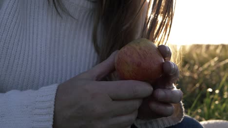 mujer sosteniendo jugosa manzana roja contra el fondo iluminado por el sol