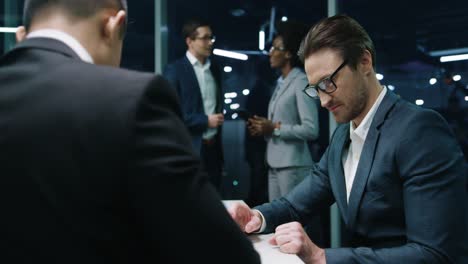 Businessmen-Sitting-At-Table-In-The-Office-And-Making-A-Deal-Shaking-Hands-In-Good-Mood