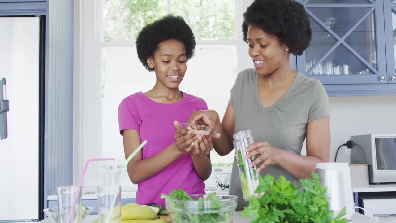 Heureuses mère et fille afro-américaines préparant une boisson saine dans la cuisine
