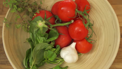 man leaving a head of garlic and some fresh basil in a bowl full of red ripe tomatoes and some fresh herbs