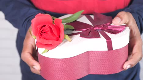 persona sosteniendo una caja de regalos en forma de corazón con una rosa roja