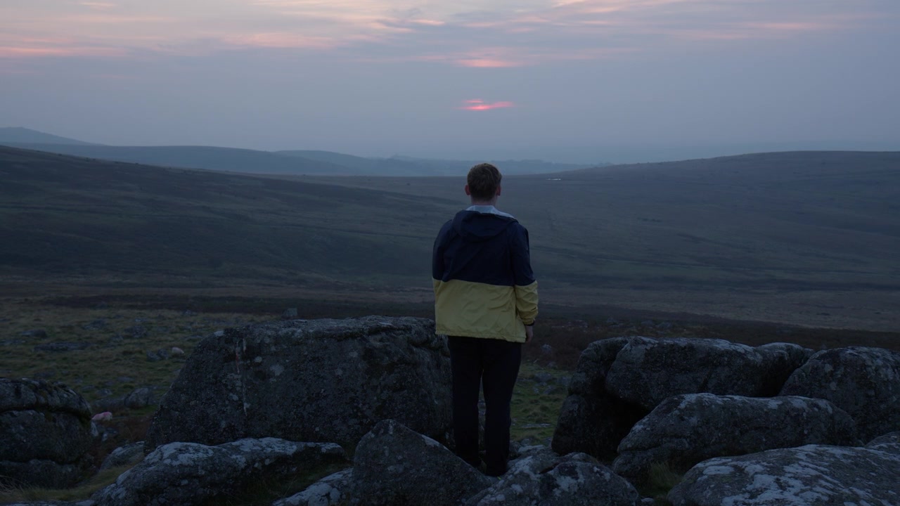 Dartmoor, Devon, Inghilterra, Regno Unito - Una persona si erge su una collina rocciosa, ammirando il vasto e tranquillo paesaggio al tramonto - Piano medio