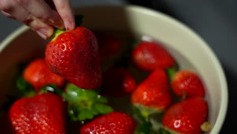 person picking a delicious organic strawberry out of a bowl