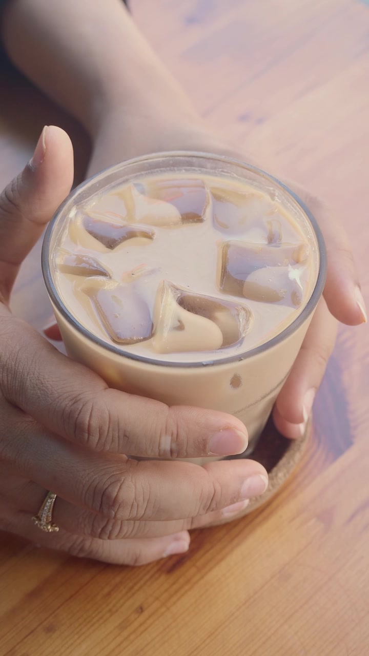 Una persona che tiene un bicchiere di caffè freddo su un tavolo di legno