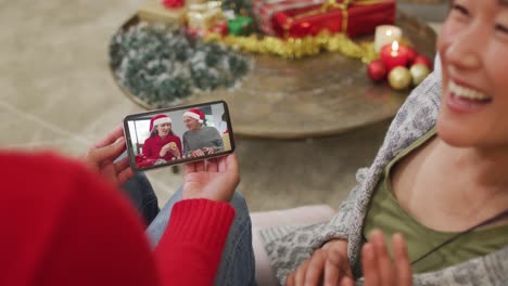 Lächelndes-Asiatisches-Paar,-Das-Sein-Smartphone-Für-Einen-Weihnachtsvideoanruf-Mit-Der-Familie-Auf-Dem-Bildschirm-Nutzt