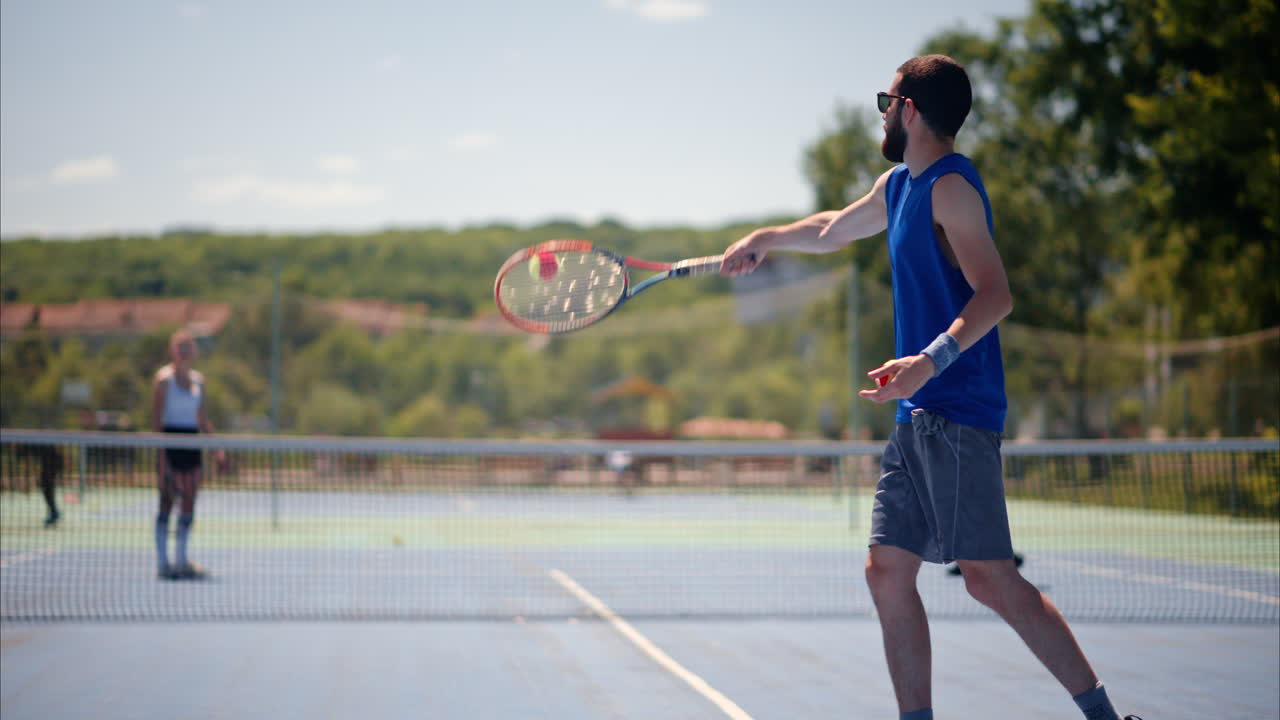 Man and woman playing tennis on a blue and green court on a sunny day