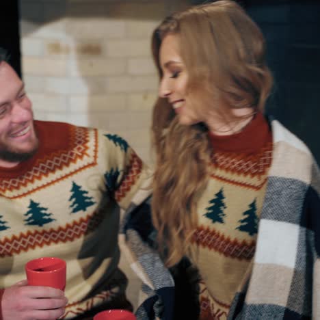 romantic couple with red mugs near fireplace. young man and woman drinking tea and chat near the the fireplace. concept of cozy home and love.