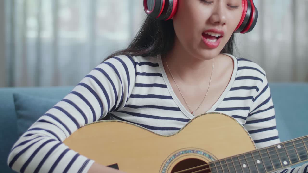 헤드폰을 들고 집에서 노래하고 기타를 연주하는 아시아 여성 작곡가의 클로즈업