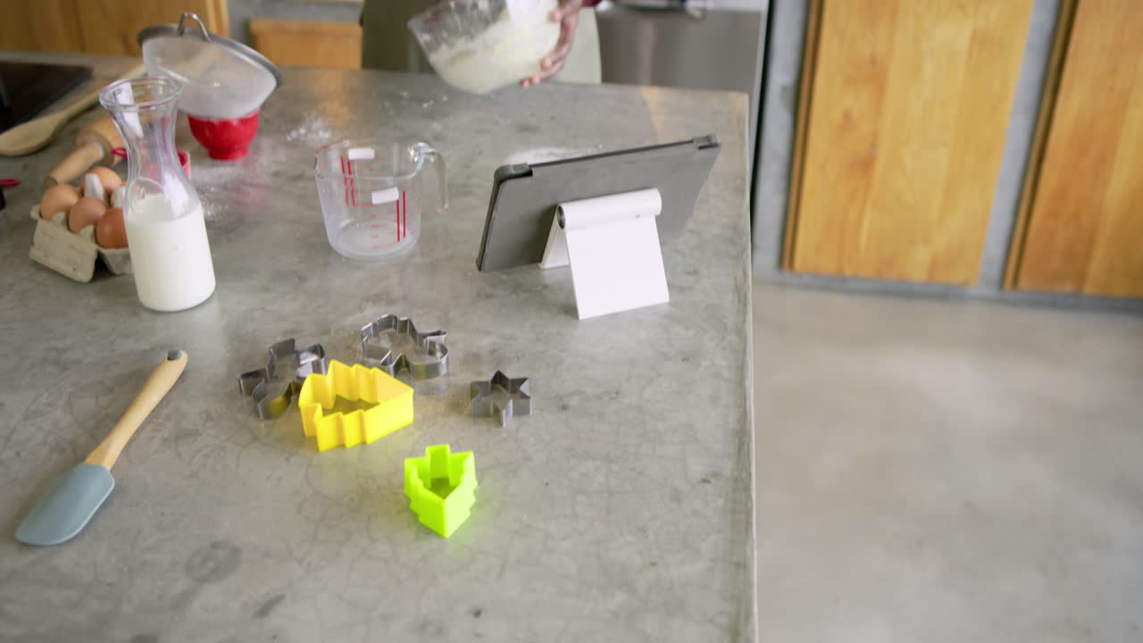 African American man whisking batter in bowl on island while consulting tablet for holiday baking