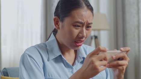 거실의 소파에 앉아있는 동안 스마트폰에서 게임을 잃는 아시아 여성의 가까운 모습