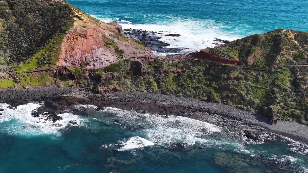 Drone glides above rugged cliffs, turquoise ocean, and dramatic coastline under bright natural daylight