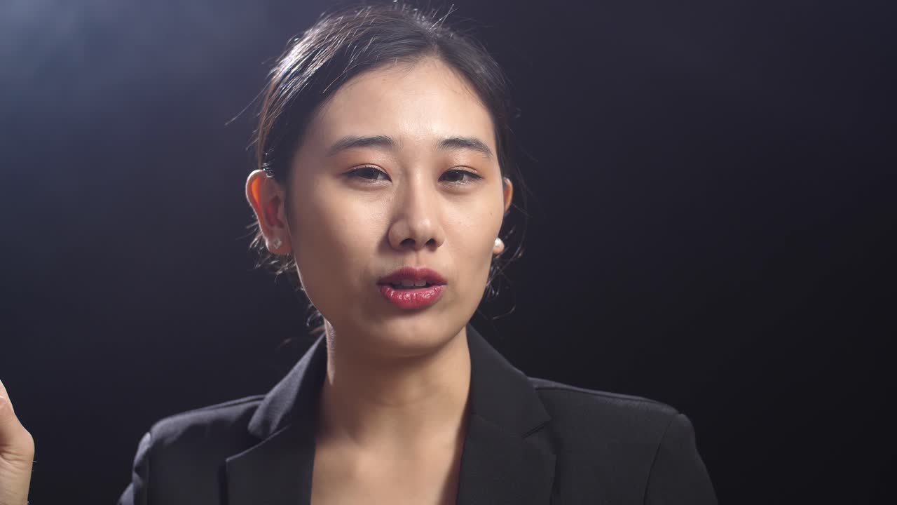 블랙 스크린 스튜디오에서 말하는 동안 지표손가락을 보여주는 비즈니스 슈트를 입은 아시아 스피커 여성의 클로즈업