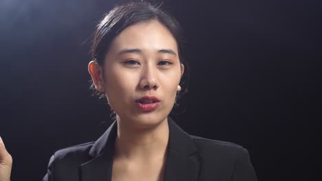 close up of asian speaker woman in business suit showing index fingers up while speaking in the black screen studio