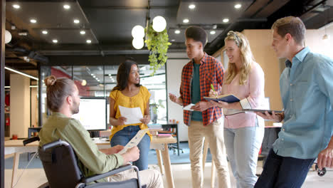 diverse male, female and disabled colleagues in discussion at casual office meeting, slow motion