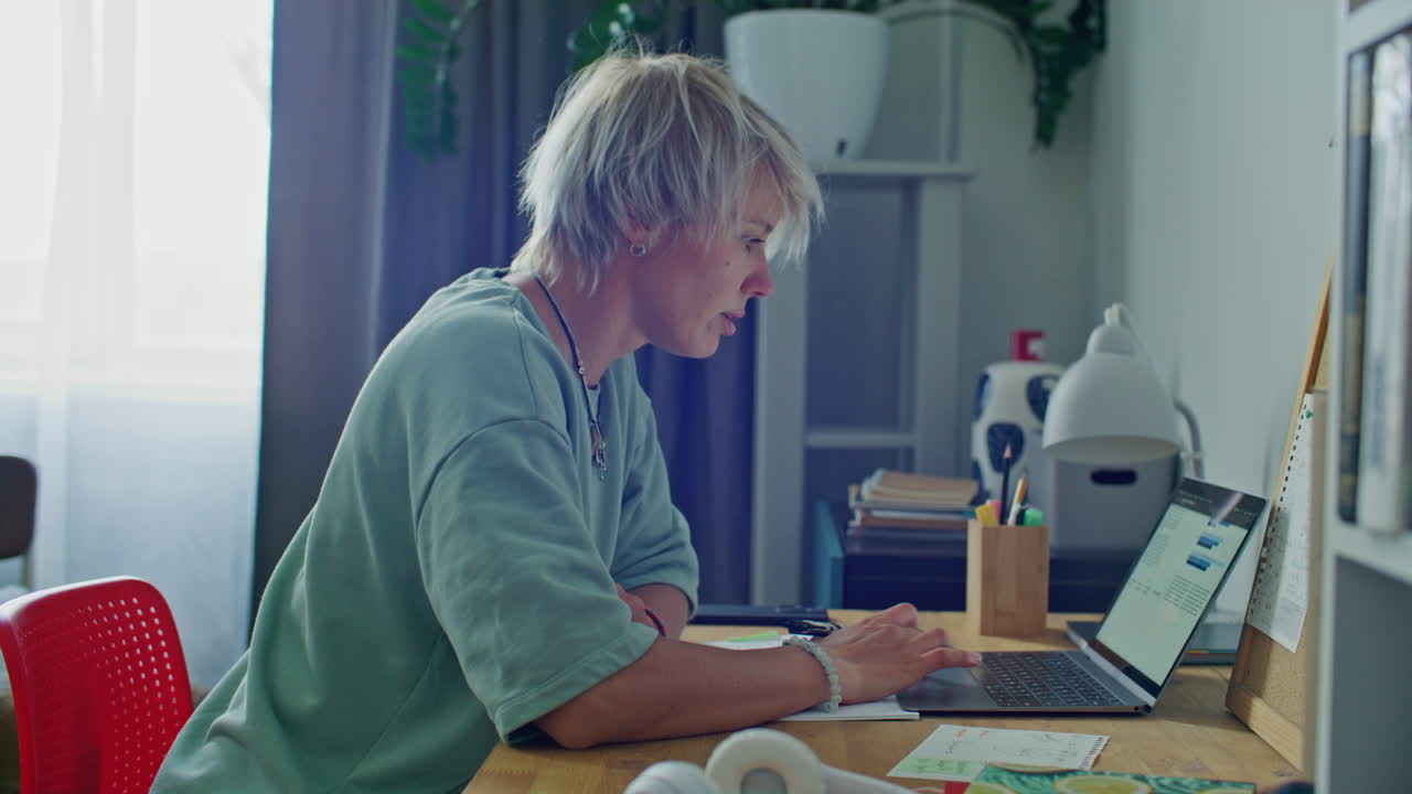 Concentrated Woman Working on Laptop and Taking Notes at Desk in Home Office